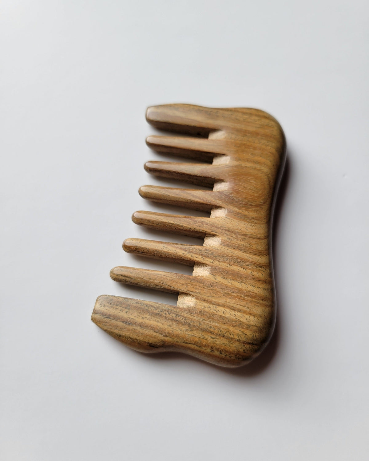 a minimalist style detangling sandalwood comb with 8 extra wide teeth. This wooden comb has a natural brown color and smooth rounded design.