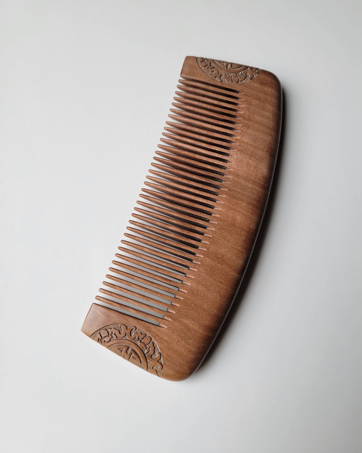 Single-piece peach wood comb shown at an angle, highlighting its polished edge, natural grain, and vintage-style carving. Natural hair care product for gifting. comes with carrying bag.