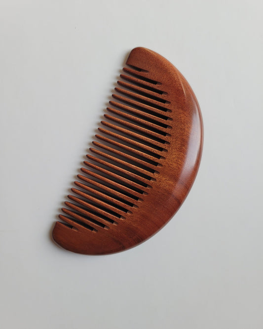 Red African Mopane wood pocket comb with smooth half-moon shape and distinctive dark striped grain