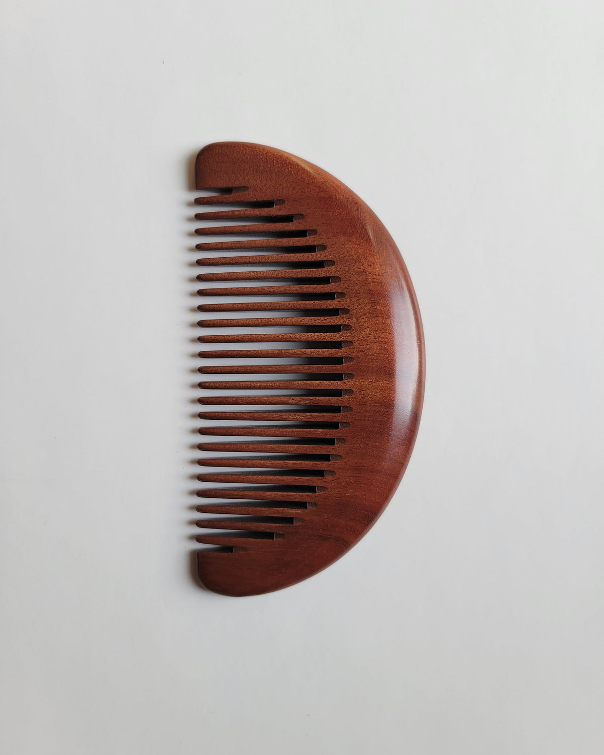 Close-up of hand-polished Mopane hardwood comb with flowing natural grain and rounded curved edges