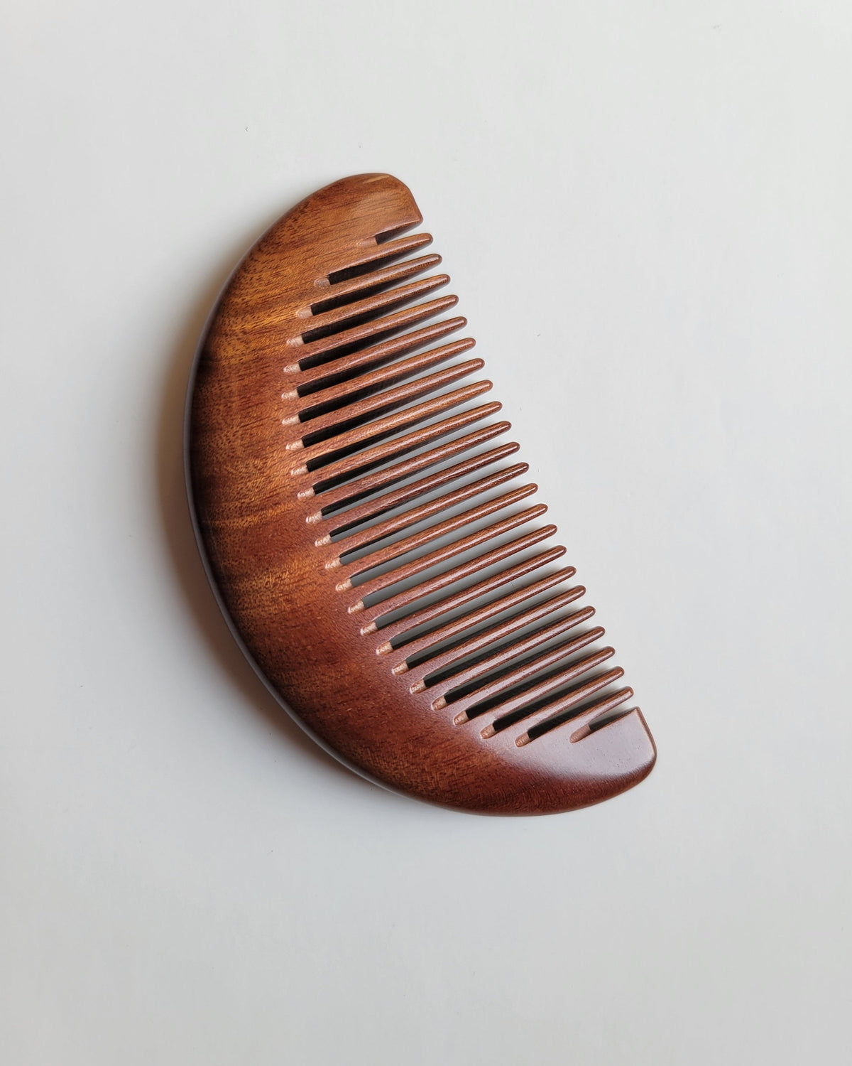 Slim half-moon pocket comb carved from a single piece of dense Mopane heartwood for travel grooming