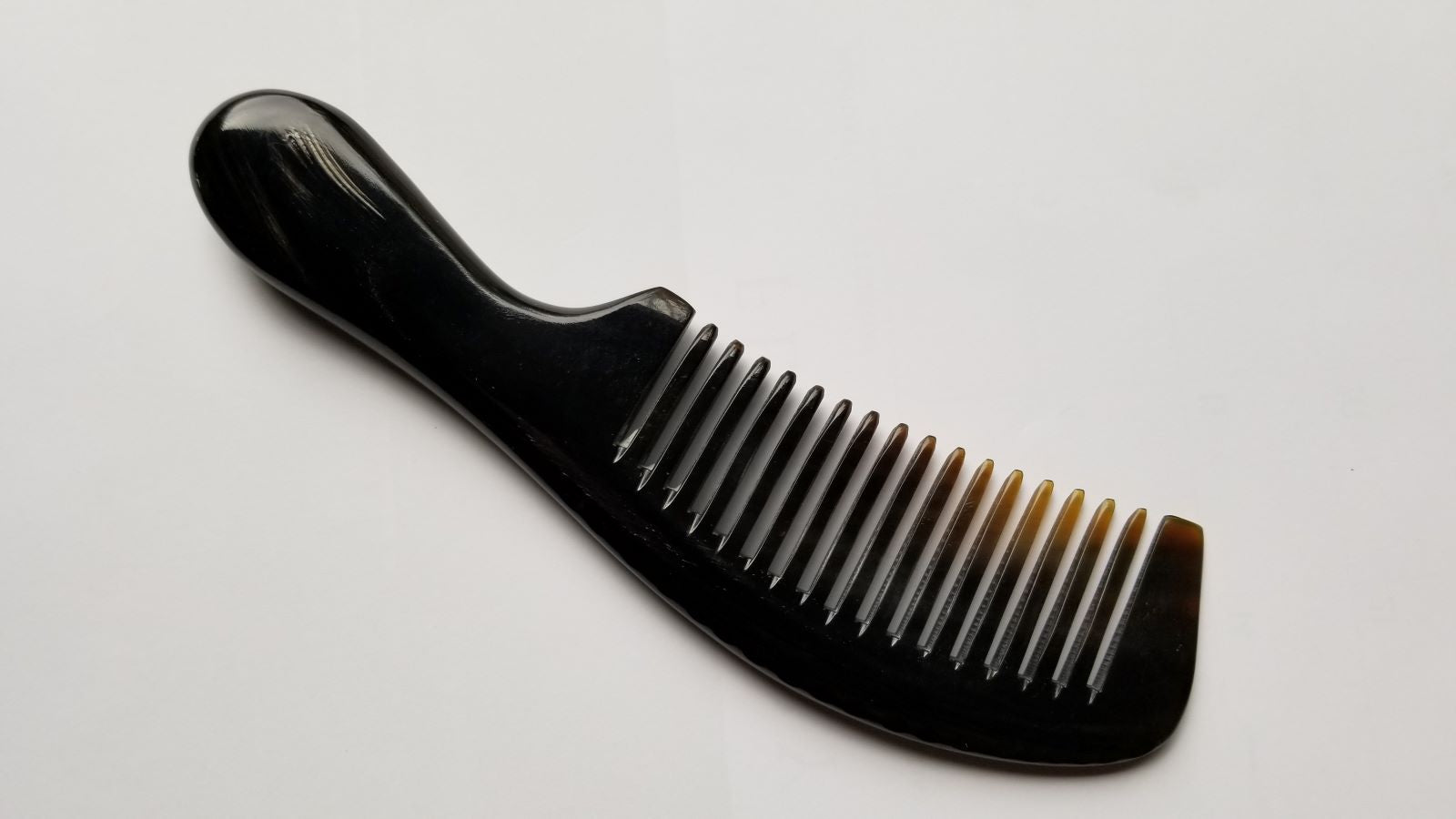 A black horn comb with a rounded handle and teeth. The comb is made of a buffalo horn, The teeth are nicely spaced and the handle is curved for easy grip.
