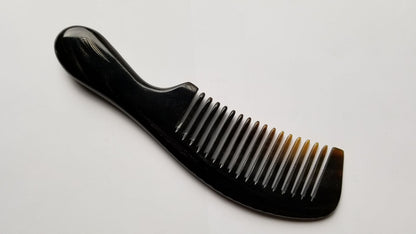 A black horn comb with a rounded handle and teeth. The comb is made of a buffalo horn, The teeth are nicely spaced and the handle is curved for easy grip.
