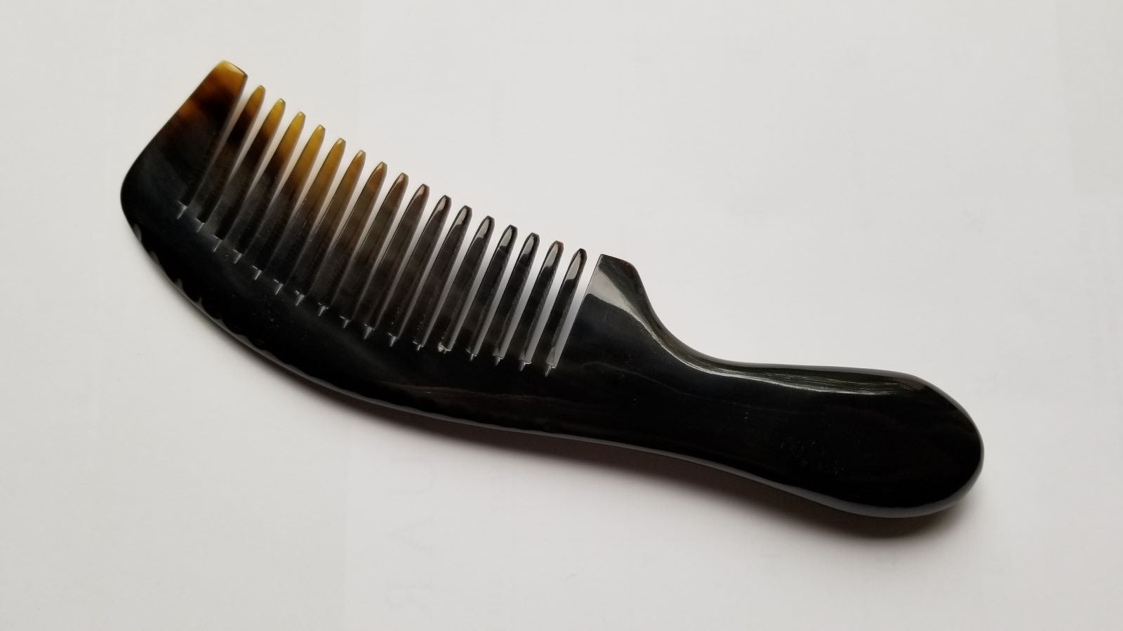 A near black comb with a curved handle and closely spaced teeth. The comb transitions from black to a translucent amber color at the tips. The handle has a smooth, ergonomic design. This hair comb is designed for grooming.