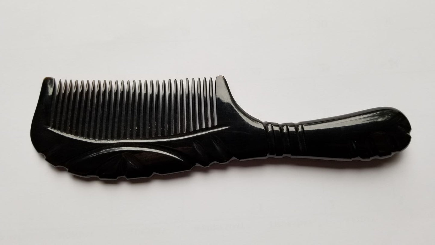 A black comb with a handle and teeth. The comb is made of a black smooth buffalo horn. The handle has a curved design and the teeth are evenly spaced.