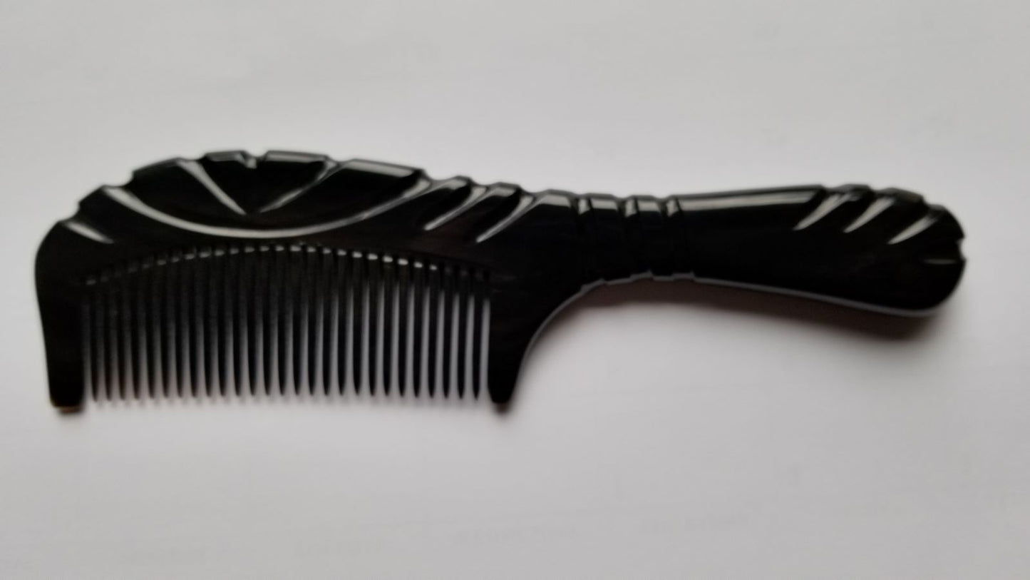 A black comb with a decorative handle and teeth. The comb features carved line designs on the handle and along the top edge. The comb is made of black buffalo horn