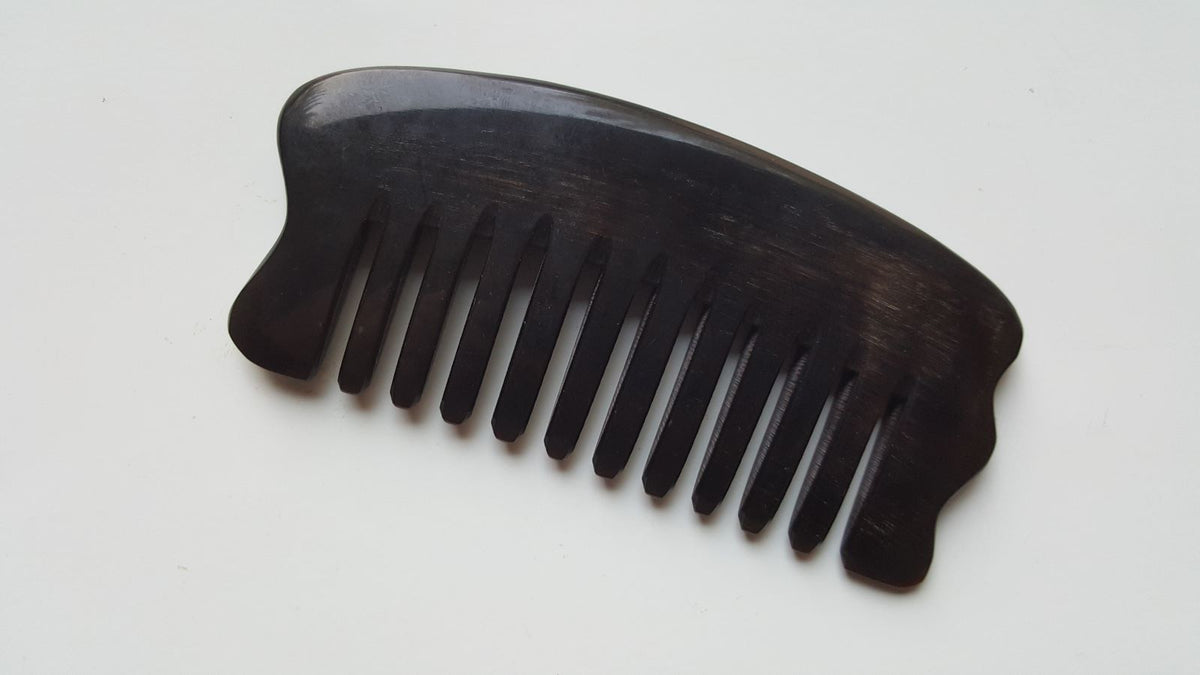 A dark brown buffalo comb with a curved handle and evenly spaced teeth. The comb is designed for hair care and grooming. The horn grain is visible, adding to the natural aesthetic. The comb is approximately 4.3 inches long.