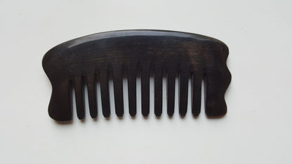 A palm size comb with a curved handle and evenly spaced teeth. The comb is made of buffalo horn, and is set against a white background. The comb's design suggests it can be used for hair care and massage.