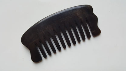 A near black comb with a curved handle and evenly spaced wide teeth. The comb is made of buffalo horn and is designed for hair grooming and as massage plate. The comb's shape is ergonomic, with a wide base and a curved top.