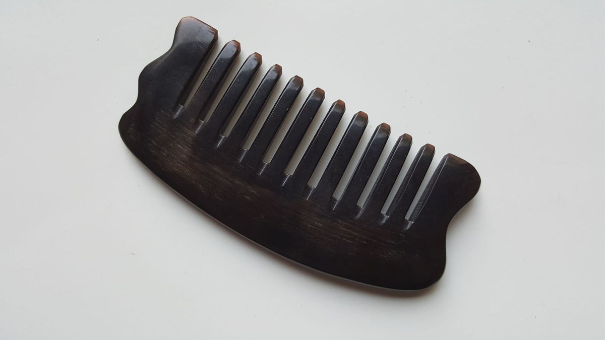 A near black buffalo horn comb with a curved handle and evenly spaced teeth. The comb is designed for hair grooming and styling.  The comb has curved handle and corners to use as massage plate.