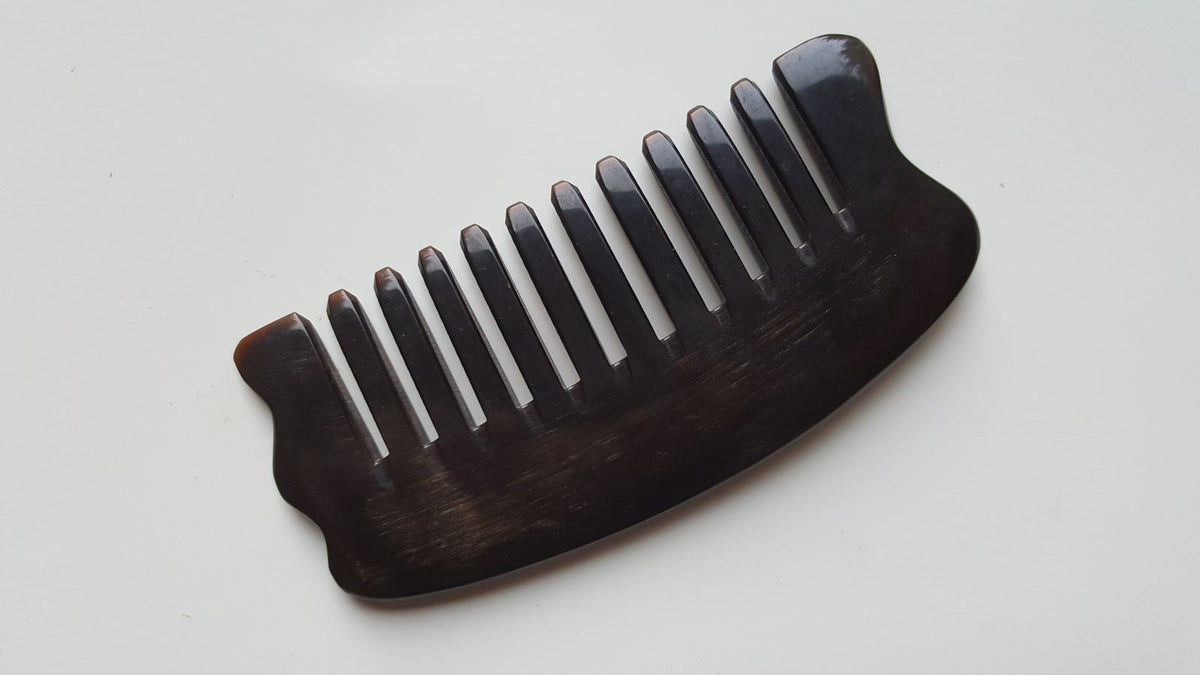 A near black comb with widely spaced teeth. The comb has a curved shape and a smooth, polished finish. The teeth are evenly spaced and the comb is made of buffalo horn. It comes with a fabric gift bag and is a great self care tool. 