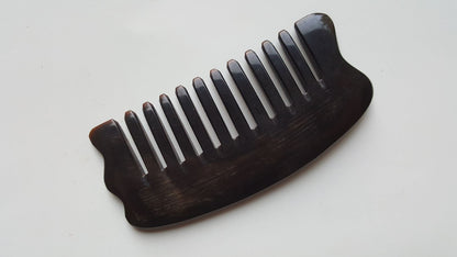 A near black comb with widely spaced teeth. The comb has a curved shape and a smooth, polished finish. The teeth are evenly spaced and the comb is made of buffalo horn. It comes with a fabric gift bag and is a great self care tool. 