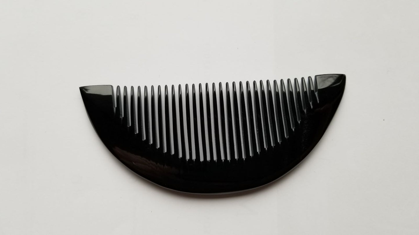 Half-moon buffalo horn comb with fine teeth facing up, natural dark horn color and grain visible
