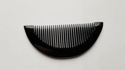 Half-moon buffalo horn comb with fine teeth facing up, natural dark horn color and grain visible