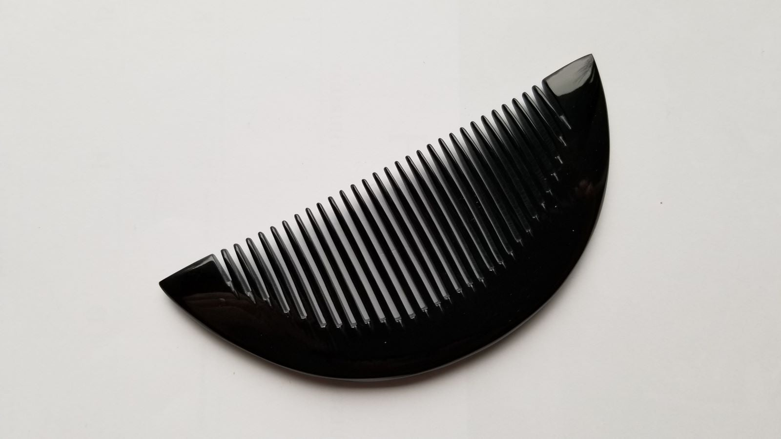 Half-moon buffalo horn comb tilted at 45 degrees, highlighting natural grain variation