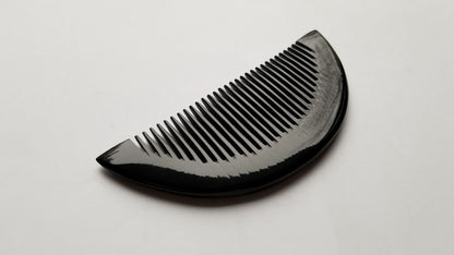 Half-moon buffalo horn comb standing upright, profile view showing slim 0.7cm thickness