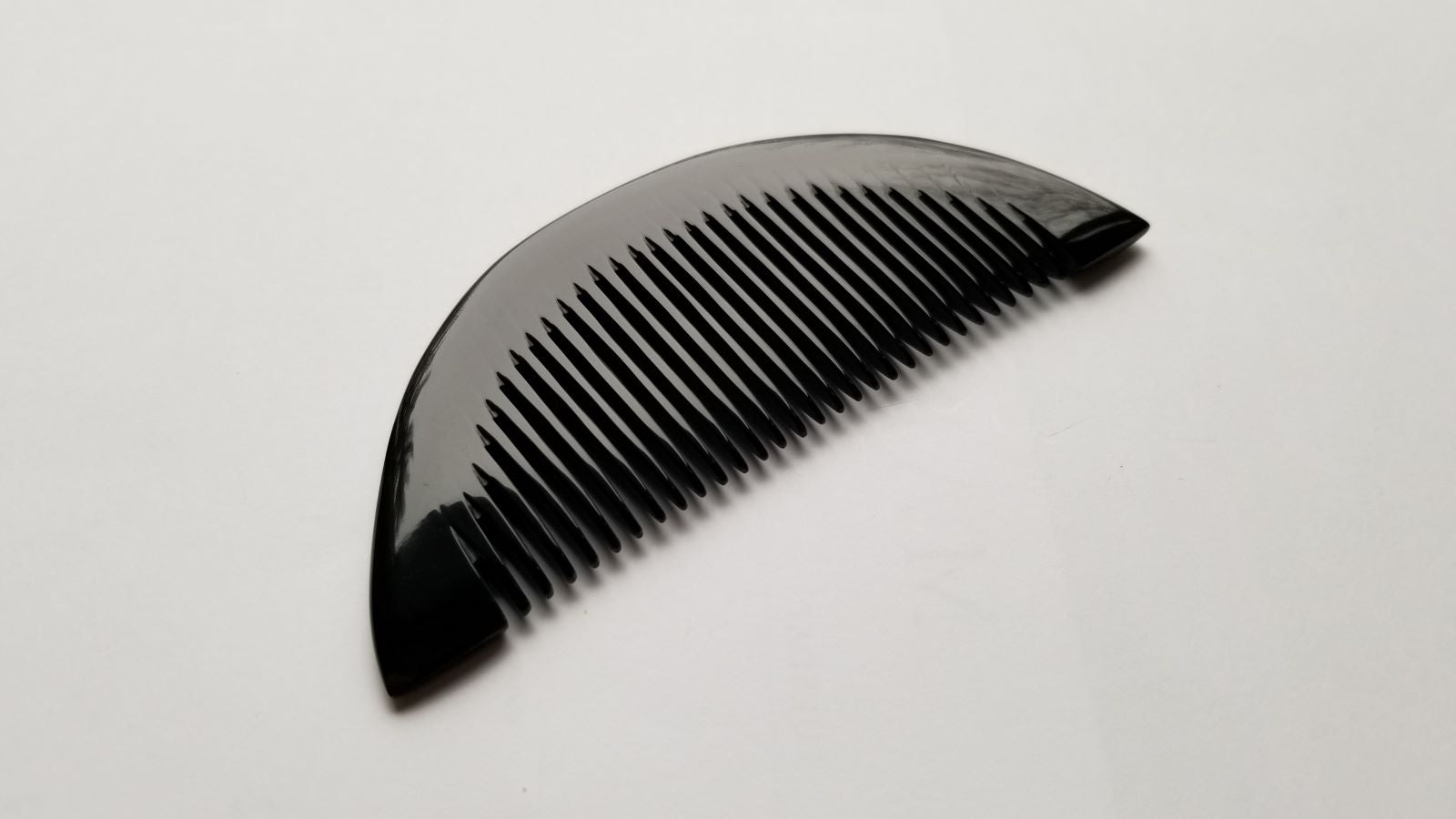 Half-moon buffalo horn comb flat lay on dark surface, contrasting natural horn tone and fine teeth
