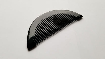 Half-moon buffalo horn comb flat lay on dark surface, contrasting natural horn tone and fine teeth