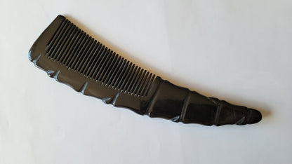 A black ox horn comb with a unique, curved design. The comb has a series of closely spaced teeth for hair grooming. The handle has a textured, ridged pattern. Great gift for dad or brothers.