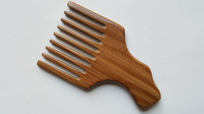 A wooden pick comb with a wide handle and multiple long teeth. The comb is made of light brown wood with a natural grain pattern.