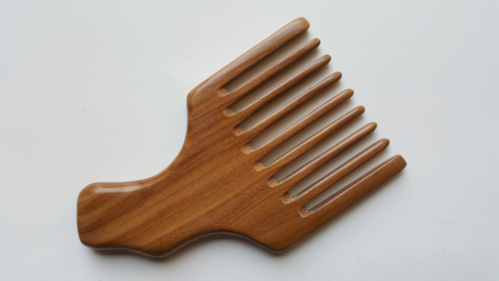 A wooden pick comb with a wide handle and a row of nicely spaced teeth. The comb is made of light brown wood with a natural grain pattern.