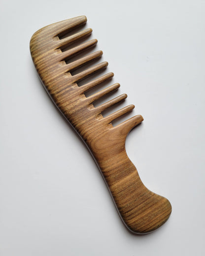 A wooden comb with a wide-tooth design. The comb is made of light brown wood with a curved handle for easy grip. The comb's teeth are evenly spaced and the overall design is smooth and polished.