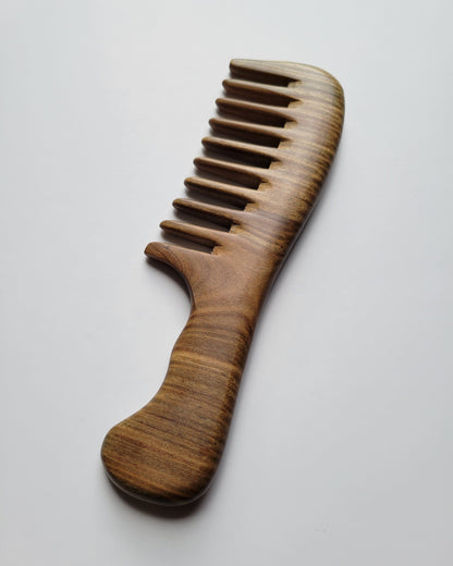 Wooden comb with wide teeth and a curved handle. The comb is made of light brown wood with visible grain patterns. The handle is ergonomically designed for easy grip and use. A beauty and grooming product.