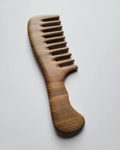 A wooden comb with a extra wide-tooth design. The comb is made of light brown wood with visible grain patterns. The handle is curved for easy grip. The comb's teeth are evenly spaced and designed for detangling hair.