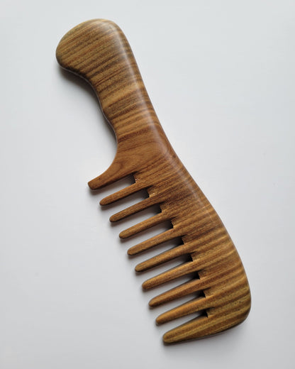 A wooden comb with a extra wide-tooth design. The comb is made of a sandalwood with visible grain patterns. The handle is curved for easy grip. The comb's teeth are evenly spaced and smooth. This hair care accessory is designed for detangling and styling.