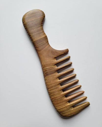 A sandalwood comb with a handle and widely spaced teeth. The comb is made of light-colored wood with a visible grain pattern. The handle is curved for easy grip, and the teeth are evenly spaced. comes with a gift bag