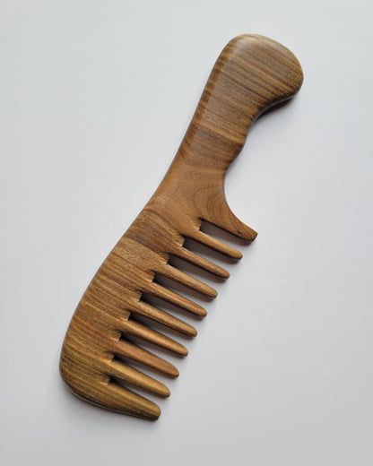 A sandalwood comb with a handle and extra wide teeth. The comb is made of a light brown wood with a visible grain pattern. The handle is curved for easy grip, and the teeth are evenly spaced. no static, eco-friendly, and gift ready. 
