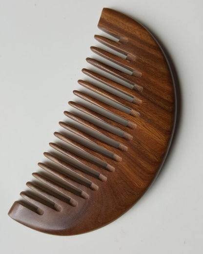 A brown wooden comb with a half-moon shape and rounded teeth. It has beautiful wood grain pattern and smooth finish.