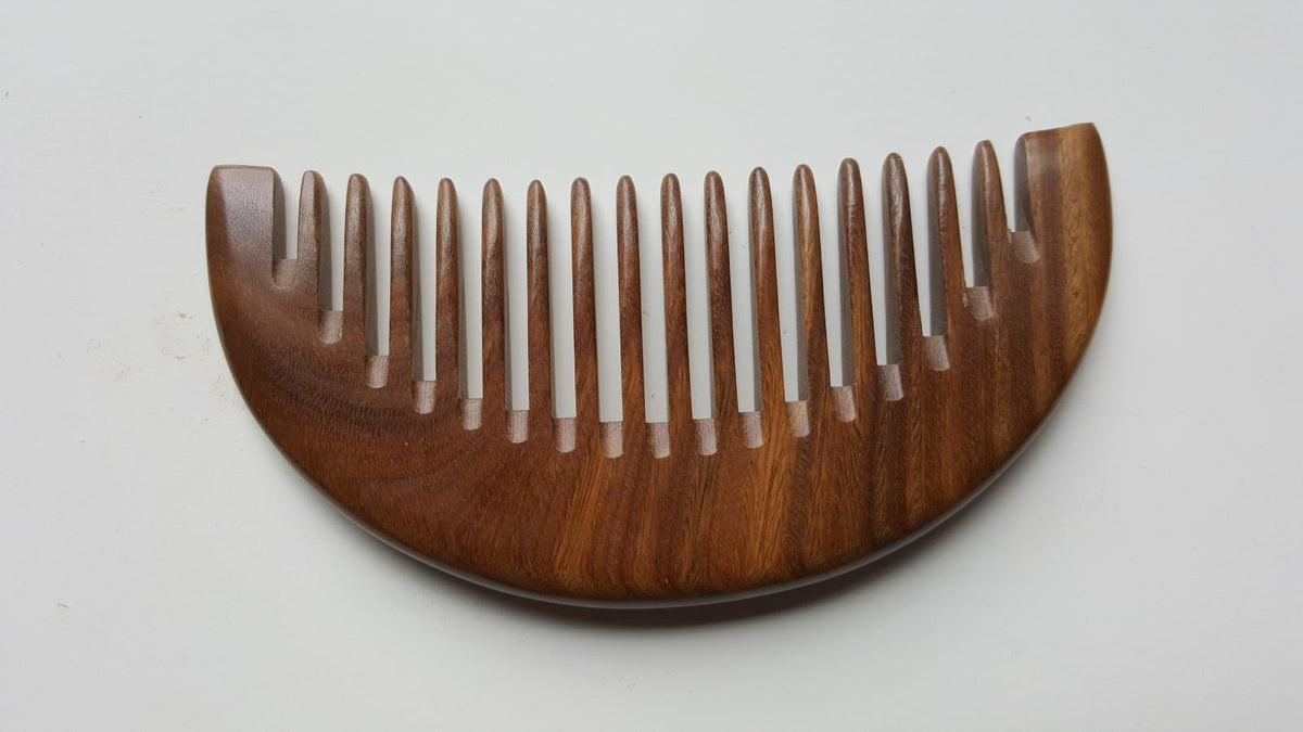 A brown wooden comb with a curved handle and wide teeth. The comb is made of natural sandalwood and has a smooth finish.