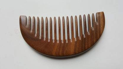 A brown wooden comb with a curved handle and wide teeth. The comb is made of natural sandalwood and has a smooth finish.