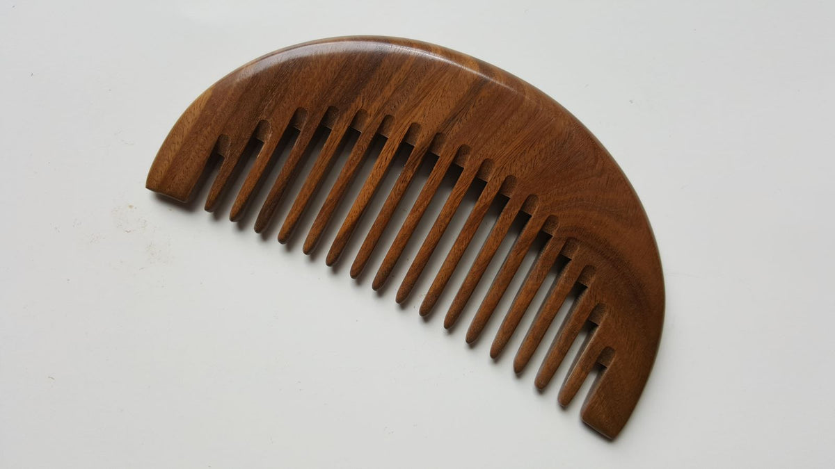 A dark brown wooden comb with a curved shape and a row of teeth. The comb is made of a natural sandalwood with a beautiful grain pattern.  Comes with fabric gift bag and great gift for love ones!