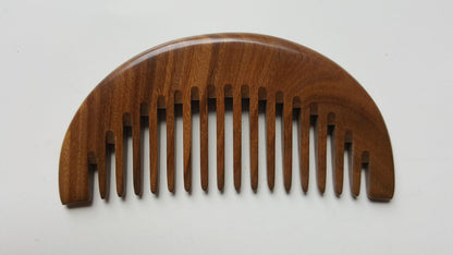 A dark brown wooden comb with a curved shape and a row of rounded teeth. The comb is made of a natural sandalwood with a beautiful grain pattern.  - front view