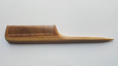 A greenish brown wooden comb with a long, thin handle. The comb has a rounded edge and a pointed tip.