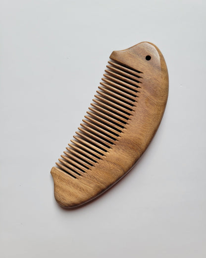 Hand carved green sandalwood fish comb for daily hair care, warm amber grain, arched fish body with tail fin and eye detail, fine tooth hair comb

