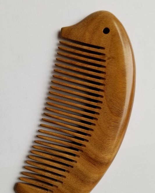 Hand carved green sandalwood fish comb for daily hair care, warm amber grain, arched fish body with tail fin and eye detail, fine tooth hair comb

