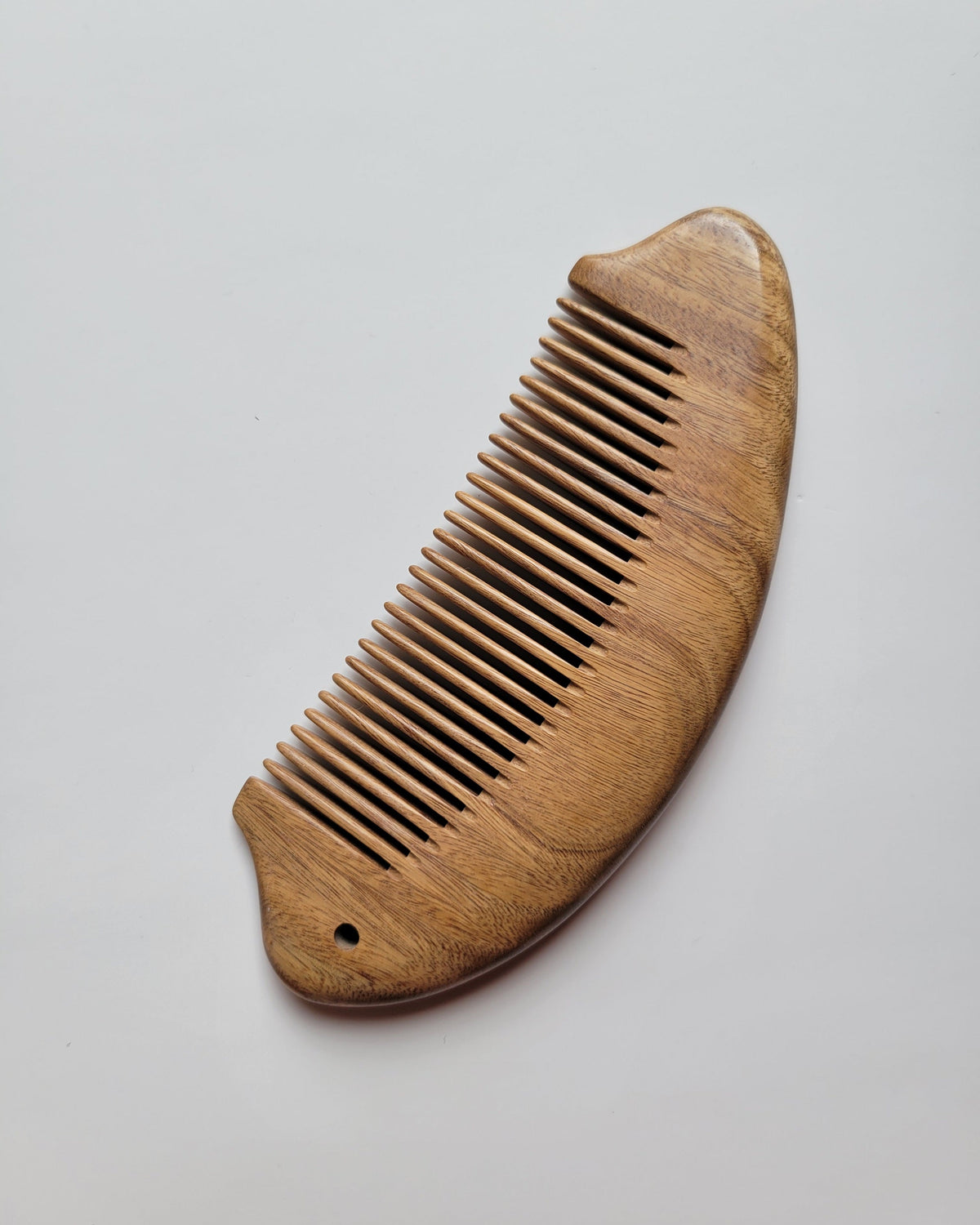 Fish silhouette sandalwood comb back view, single-piece green sandalwood construction, warm amber grain, anti-static wood hair comb
