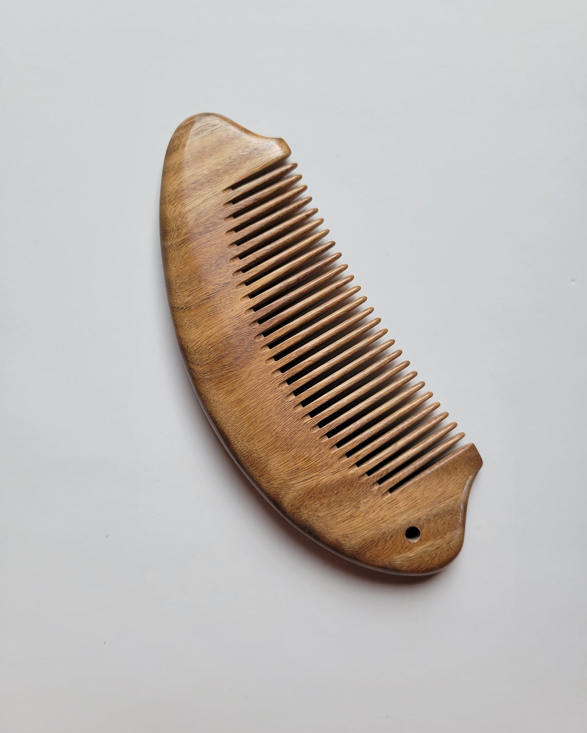 Hand carved fish comb side profile, green sandalwood sculptural form, tail fin and arched back detail, fine tooth grooming comb