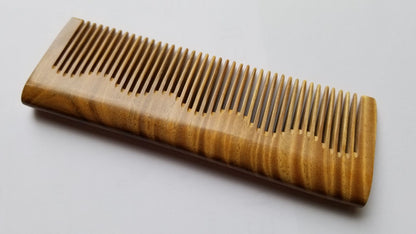 Handcrafted sandalwood comb flat lay, angled view showing natural olive-to-green wood grain — Arakicrafts