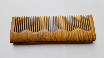 A wooden comb with a natural wood grain pattern. The comb has a rectangular shape with closely spaced fine teeth. The design features a wavy edge on one side. The comb is made of light brown wood. This wood comb works for all hair types and beard, — Arakicrafts