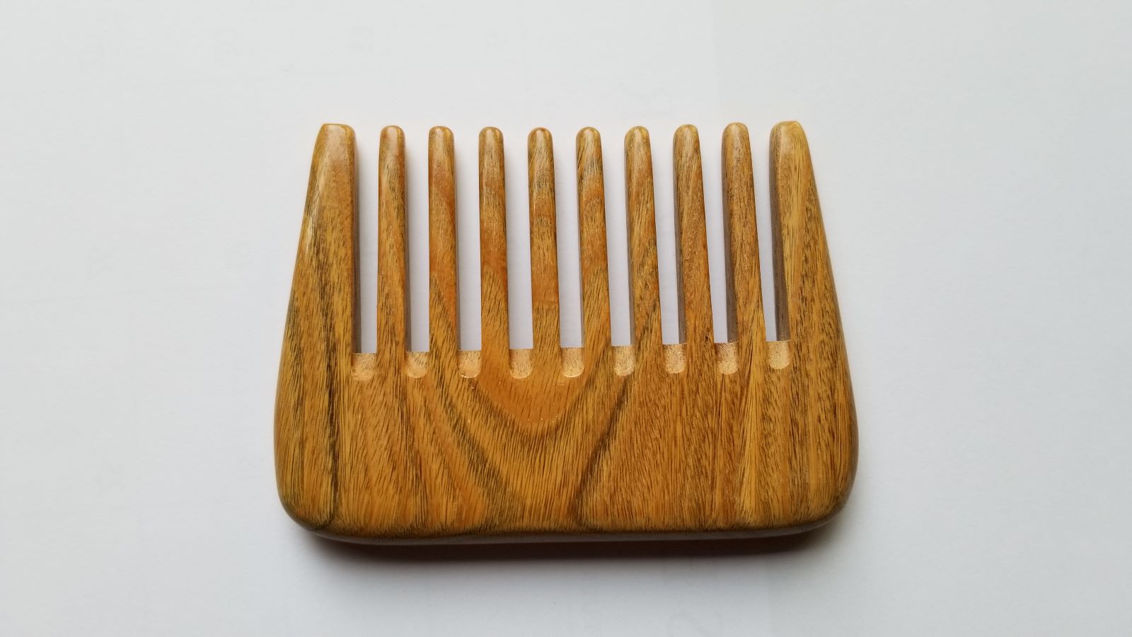 A wooden comb with a natural wood grain finish. The comb has a rounded shape and wide teeth.