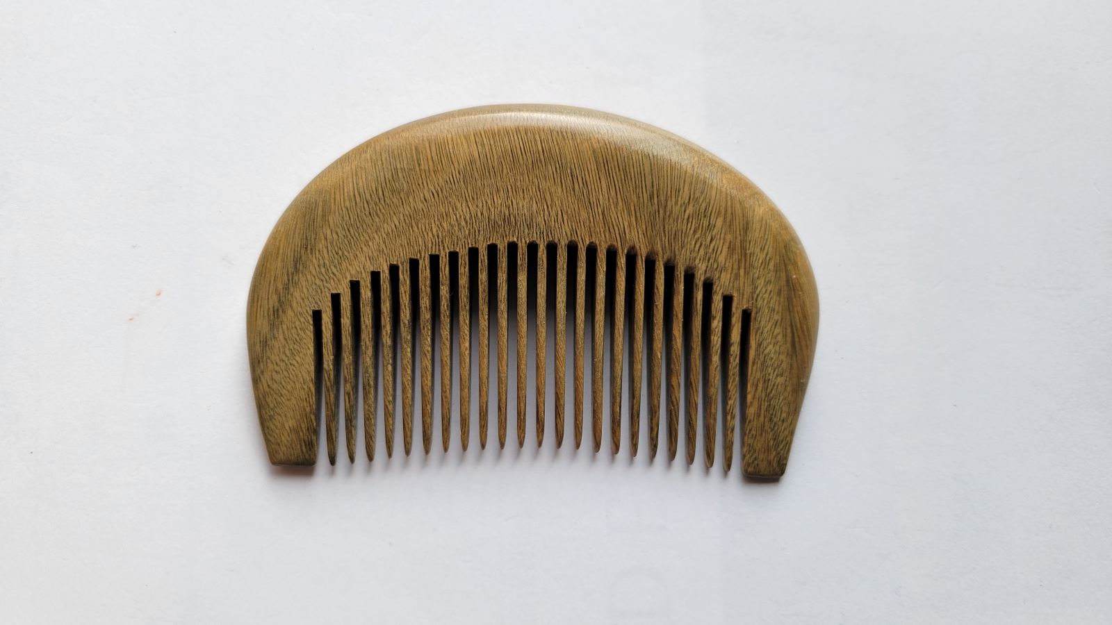 A mini wooden comb with a curved handle and closely spaced teeth. The comb is made of light brown wood and is set against a white background. The comb's design is simple and functional.