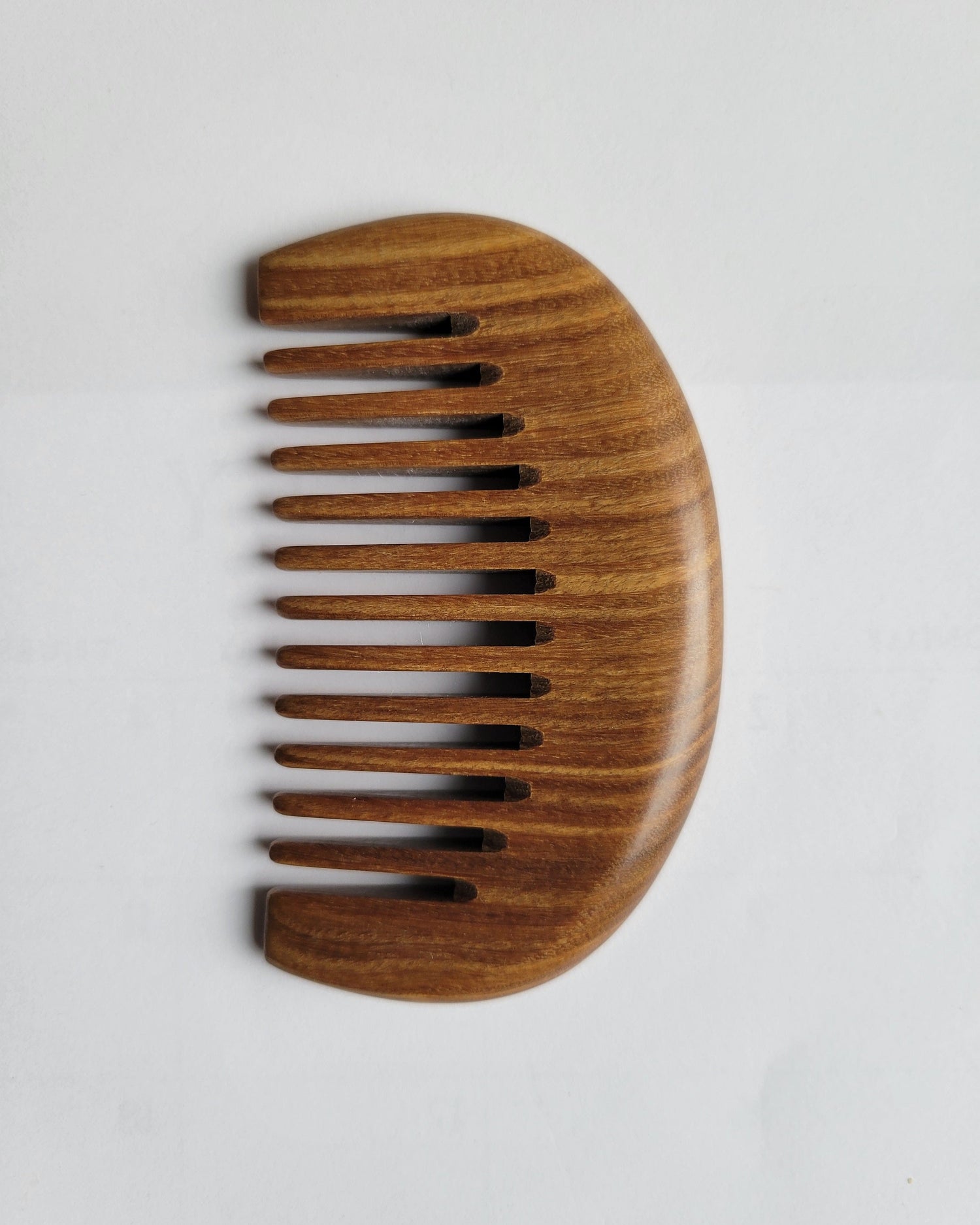 A small wooden comb with a curved handle section and a row of teeth. The comb is made of dark brown sandalwood with a natural grain pattern.