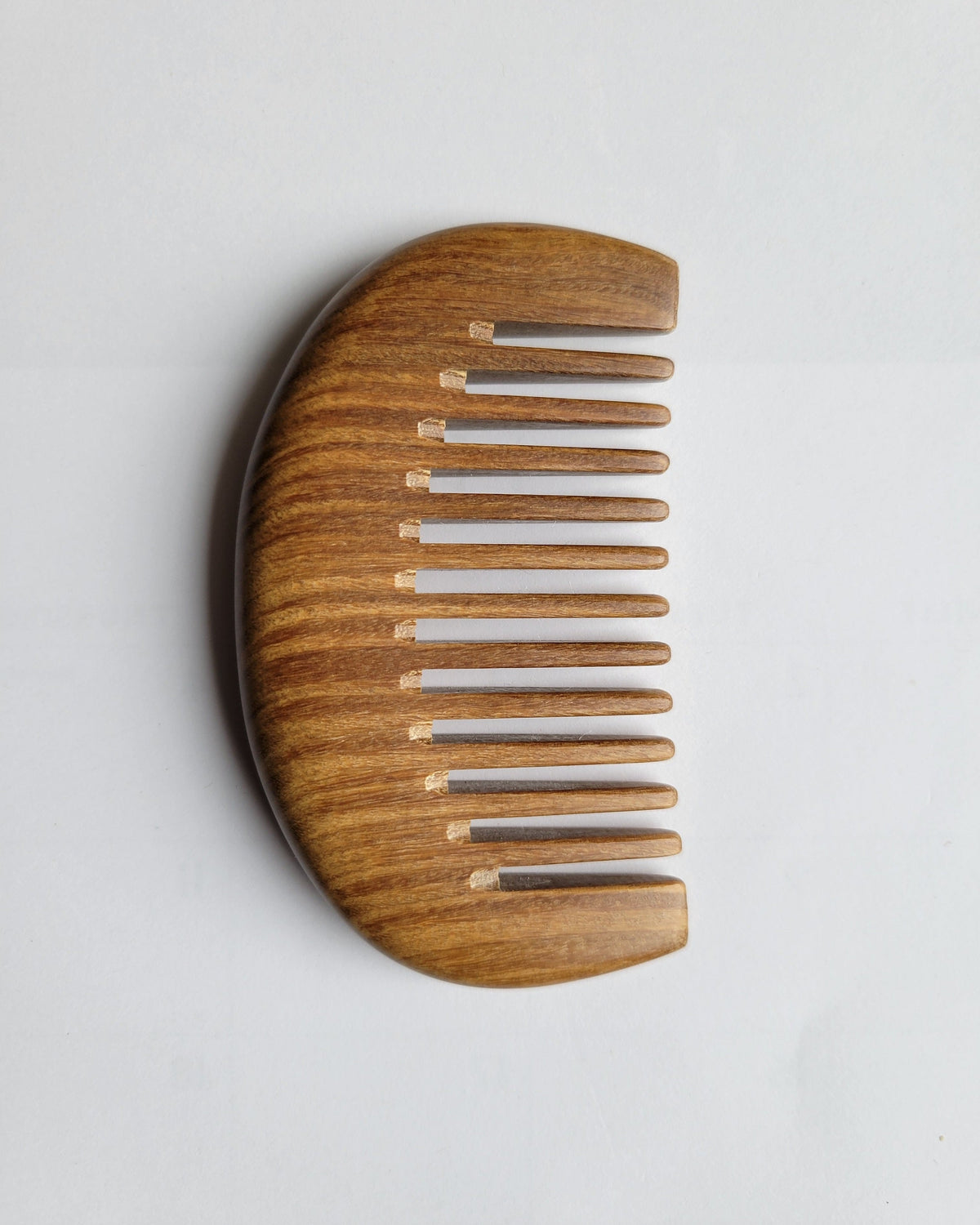 A pocket size wooden comb with a curved handle section and a row of hand polished teeth. The comb is made of a sandalwood with a natural grain.