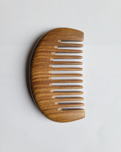 A pocket size wooden comb with a curved handle section and a row of hand polished teeth. The comb is made of a sandalwood with a natural grain.