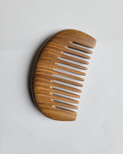 A mini wooden comb with a curved shape top and fine teeth. The comb is made of sandalwood comb with visible grain. Perfect gift for her!