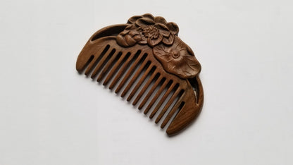 A brown wooden comb with a carved floral design. The comb is shaped like a crescent moon and has a decorative floral design on the back.